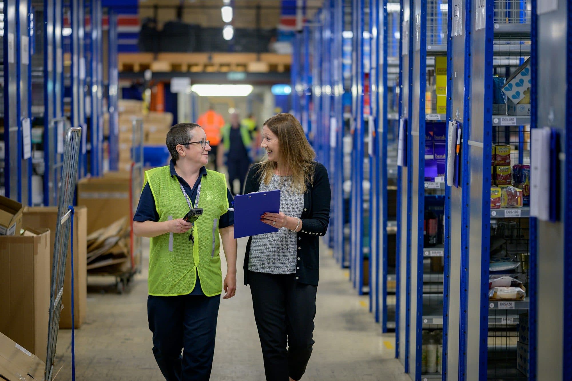 Two people walking through a warehouse aisle, one holding a clipboard